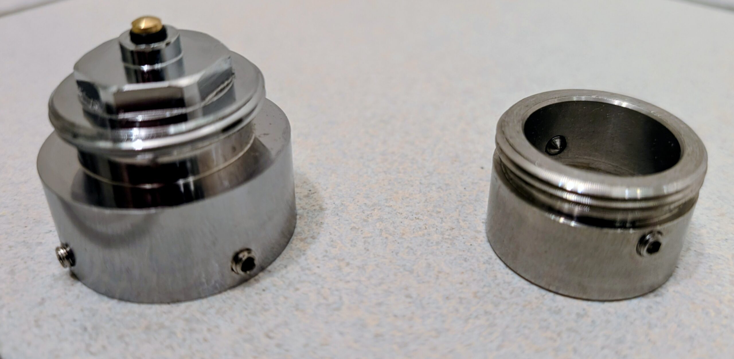 Zwei Metalladapter nebeneinander auf einer neutralen Fläche, Madenschrauben sichtbar